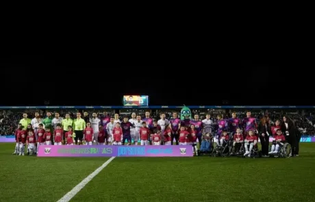 Los jugadores de dos equipos de fútbol posan con niños, algunos en silla de ruedas, tras una pancarta de sensibilización sobre las enfermedades raras.