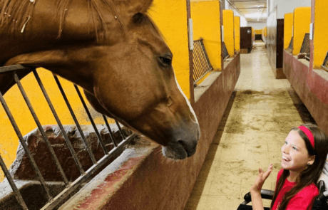Carolina, en su silla de ruedas, saluda a un caballo que asoma la cabeza en las cuadras.