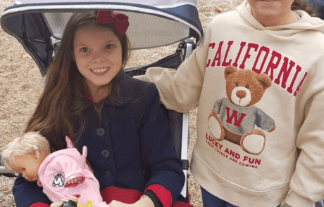 Carolina, en su silla adaptada y con una muñeca en brazos, en el parque junto a su mejor amiga Patricia.