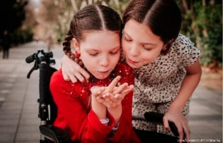 Carolina, en su silla de ruedas, y su hermana Isabel soplan juntas un puñado de purpurina.
