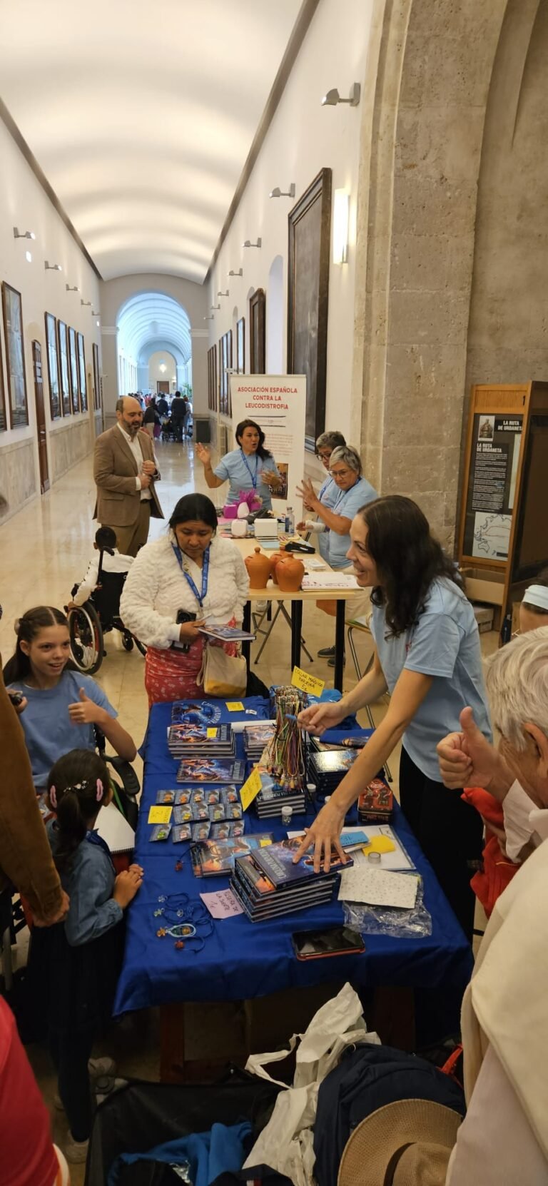 Stand mit Exemplaren von „Carolina Purpurina“ und Schmuckperlen vor dem Roll-up der Asociación Española contra la Leucodistrofia.
