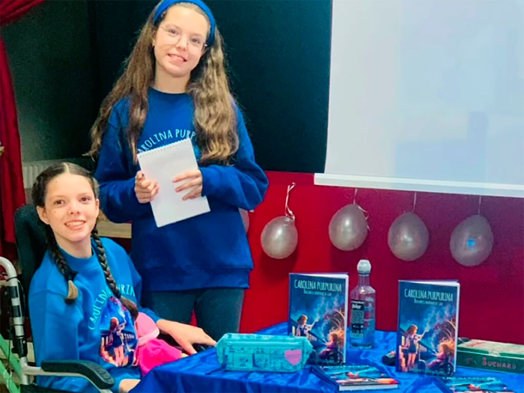 Isabel und Carolina neben dem Büchertisch während der Begegnung in der CEIP Marqués de Valero in Béjar.