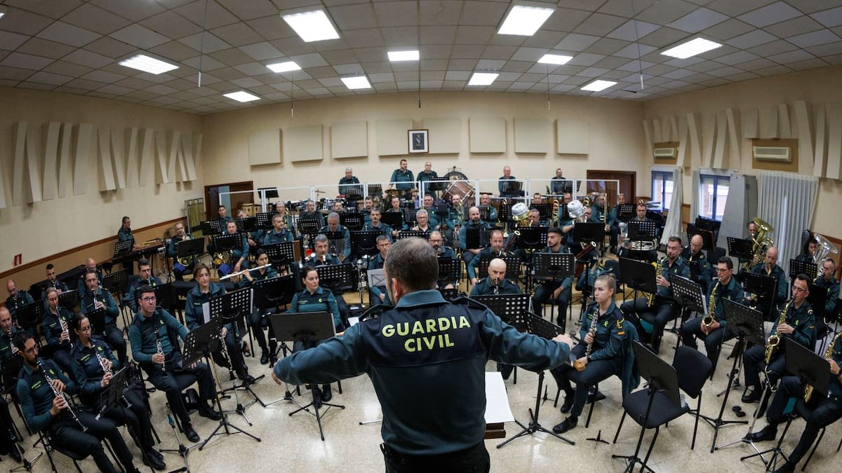 Un director con chaqueta de la Guardia Civil, de espaldas, dirige el ensayo de la banda que dio un concierto a beneficio de la asociación.