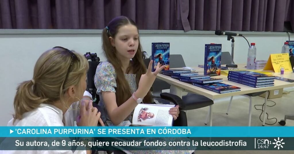 Reportage de Canal Sur à Cordoue : une fillette assise, livre ouvert, parle avec une femme ; derrière, la table chargée d’exemplaires du livre.